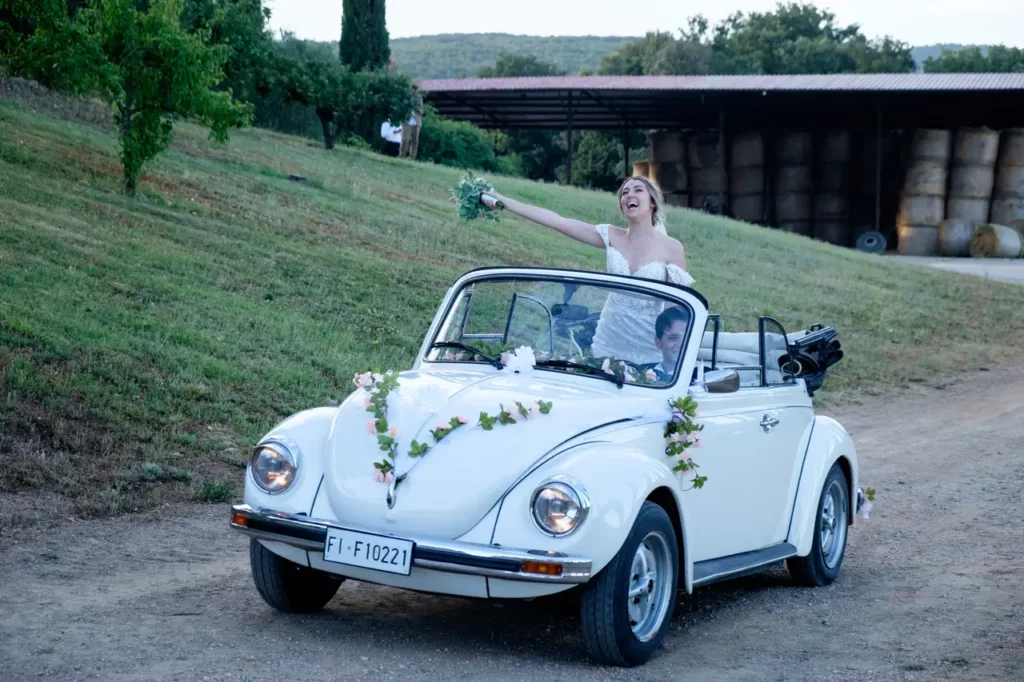 Gli sposi, su un maggiolone bianco, arrivano al ricevimento.
